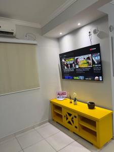 een kamer met een gele tafel en een tv aan de muur bij Mariscal 2 quartos 3 banheiros -SOBRADO AMENDOEIRA in Bombinhas