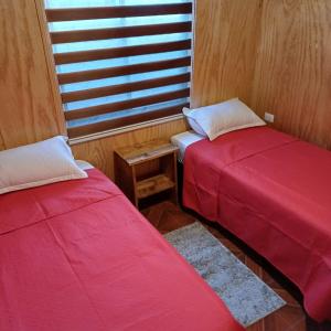 2 rode bedden in een kamer met een raam bij Refugio las Mariposas Chillán in Chillán