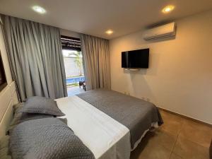 a bedroom with a bed and a tv on the wall at Pipa Beleza Suítes in Pipa