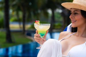 a woman in a hat holding a drink by a pool at Villas La Mar in Monterrico