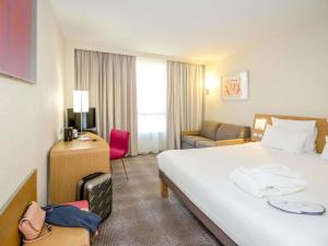 a hotel room with a large bed and a chair at Novotel Perpignan Nord Rivesaltes in Rivesaltes