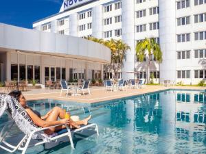 a woman sitting in a chair next to a swimming pool at Novotel Sao Jose dos Campos in São José dos Campos