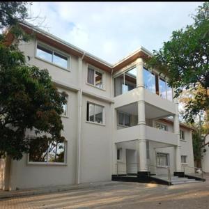 a large white building with trees in front of it at Tiny Card Milimani Homes in Kisumu