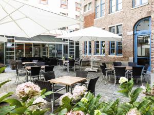 un patio con tavoli, sedie e ombrelloni bianchi di Novotel Gent Centrum a Gand