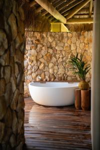 a bath tub in a room with a stone wall at Primitivo Hotel & Villas in Passo de Camarajibe