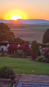 a sunset over a garden with the sun setting in the distance at Ashley's Cottage in Himeville