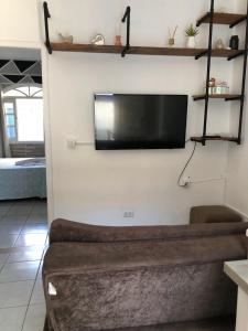a living room with a couch and a flat screen tv on a wall at Kitnet centro de bombinhas in Bombinhas