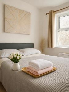 een bed met een dienblad met handdoeken en een vaas met bloemen bij Crown Heights Executive Apartment in Manchester