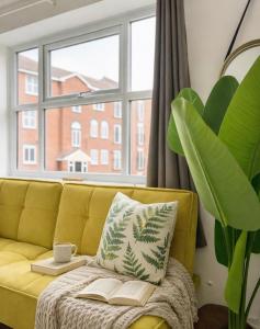 een gele bank voor een raam met een boek bij Crown Heights Executive Apartment in Manchester