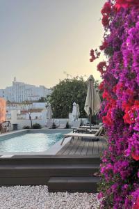 een zwembad met stoelen, parasols en paarse bloemen bij Fishermans Beach Suites & Rooms Albufeira in Albufeira