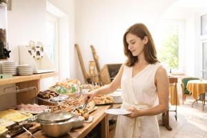 a woman holding a plate in a kitchen with food at Hotel Comfort Erica Dolomiti Val d'Adige in Salorno