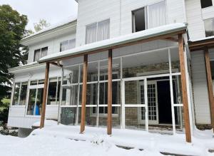 a building with a covered porch in the snow at Kamoshika Lodge Hakuba in Minami Otari