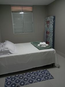 a bed with white sheets and a window and a rug at Conforto setor Oeste garagem 505 in Goiânia