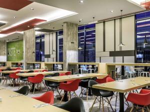 a dining room with tables and chairs and windows at ibis Bangkok IMPACT in Nonthaburi