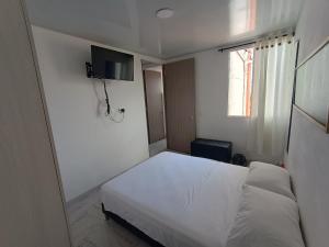 een slaapkamer met een wit bed en een televisie aan de muur bij Apartamento en Ibagué Campestre in Ibagué