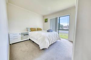 een slaapkamer met een bed en een groot raam bij Relaxing 3BR Home by Wattle Downs Reserve in Auckland