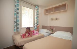 Ein kleines Mädchen, das auf einem Bett liegt und ein Buch liest. in der Unterkunft Domaine Résidentiel de Plein Air Odalys Les Demoiselles in Saint-Hilaire-de-Riez