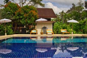 a swimming pool with chairs and umbrellas next to a house at Lanta White Rock Resort in Ko Lanta