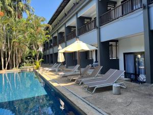 a pool with lounge chairs and an umbrella next to a building at Khao Lak - Loft Suite with 2 king size beds, bathroom with bathtub in Khao Lak