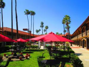une cour avec des tables, des parasols rouges et des palmiers dans l'établissement Hotel Saddleback, à Norwalk