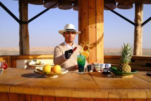 a man in a hat standing at a table with a drink at SEVEN SAINTS Lodges in El Karia +28 photos