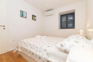 a white bedroom with a bed and a window at Apartments Rialto in Veli Lošinj