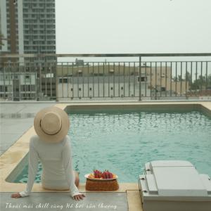 a person in a hat sitting next to a swimming pool at Mira Grand Hotel Quy Nhơn in Quy Nhon