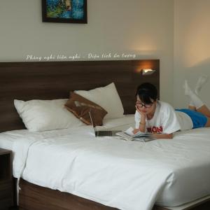 a woman laying on a bed reading a book at Mira Grand Hotel Quy Nhơn in Quy Nhon