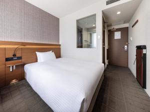 a bedroom with a large white bed and a door at Nishitetsu Hotel Croom Hakata in Fukuoka