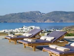 Een rij ligstoelen op een terras met uitzicht op het water. bij Lithos Luxury Rooms (Adults Only) in Adamas
