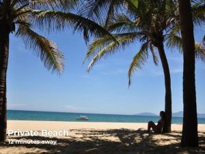 a woman sitting on the beach between two palm trees at Eco Hotel Hoi An in Hoi An