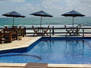 a swimming pool with two tables and umbrellas next to the ocean at Pousada Porto Meu Amor in Porto De Galinhas