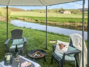 a table and chairs under a tent with a view of a river at Harperfield Chalet in Lanark