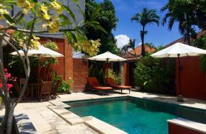 a swimming pool with umbrellas and chairs next to a house at Merpati - Studios in Sanur