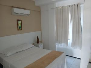 a white bedroom with a bed and a window at Brisa Brasil Residence in Fortaleza
