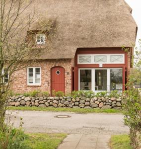 a brick house with a red door and a stone wall at Foftein in Borgsum