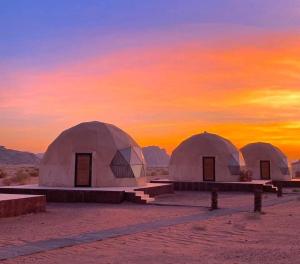 drie koepels in de woestijn met een zonsondergang op de achtergrond bij Desert Stars Bubble Camp Wadi Rum in Wadi Rum