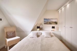 a white bedroom with a bed and a chair at Hüs Freesenborg in Oldsum
