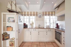 a kitchen with white cabinets and a clock on the wall at Reethüs Marta - rechts in Utersum +10 photos