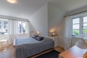 a white bedroom with a bed and two windows at Reetdachhaus Hedehusum in Hedehusum