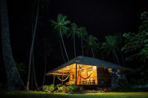 a cabin lit up at night with palm trees in the background at Kita Surf Resort in Lasikin