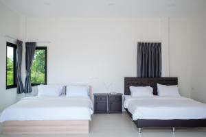 two beds in a bedroom with white walls and windows at The Rock Coco Villa 2 in Ban Sai Mat