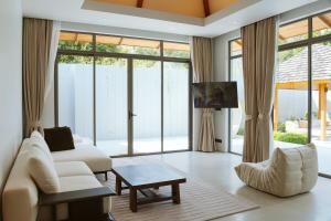 a living room with white furniture and large windows at Anchan Flora Luxury 2BR Pool Villa in Thalang