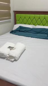 een wit bed met een groen hoofdeinde en handdoeken erop. bij Transient Room in Dasmariñas