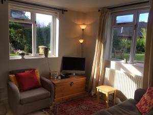 a living room with a chair and a tv and two windows at Leadenham Cottage in Oakham