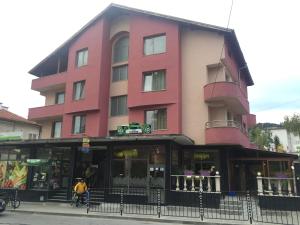 a pink building with a person on a bike in front at Family Hotel Neliya in Velingrad