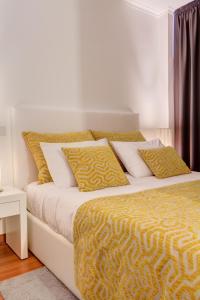 Cama con sábanas y almohadas amarillas y blancas en Bracara Guest House "Campo Novo", en Braga