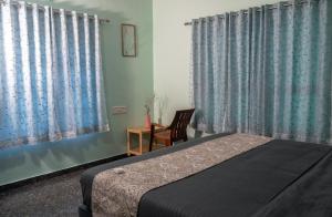 a bedroom with a bed and a chair and curtains at WildWood Stay in Madikeri