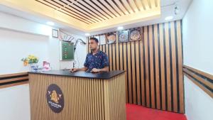 un uomo è in piedi davanti a un bancone in una stanza con una parete di legno di Hotel Golden Bird a Dhaka