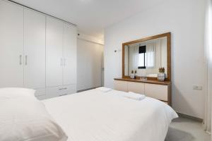 een witte slaapkamer met een groot bed en een spiegel bij Spacious Family Luxury Getaway in Ashdod